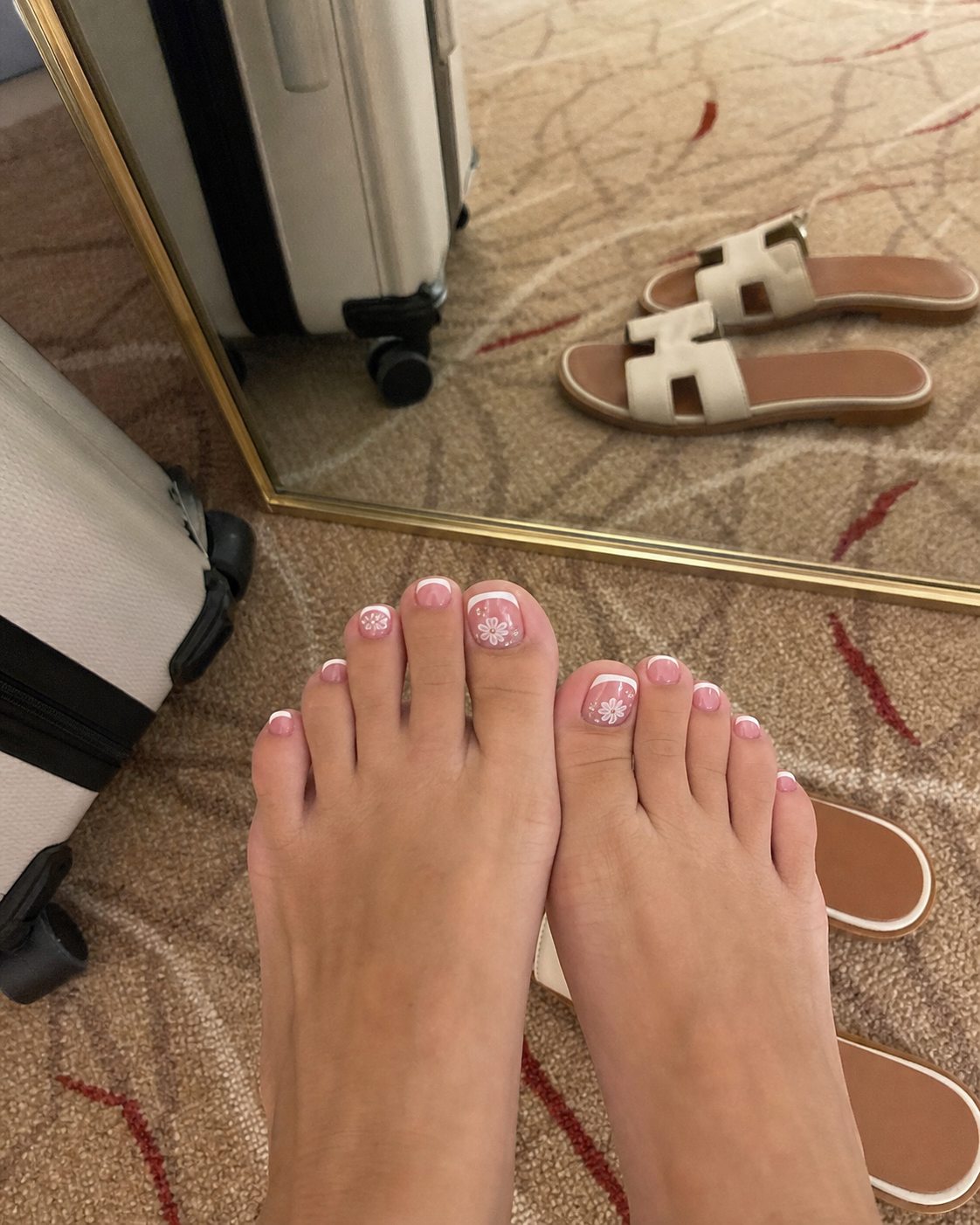 Hotel mirror phone photo of neutral press-on nails with a suitcase