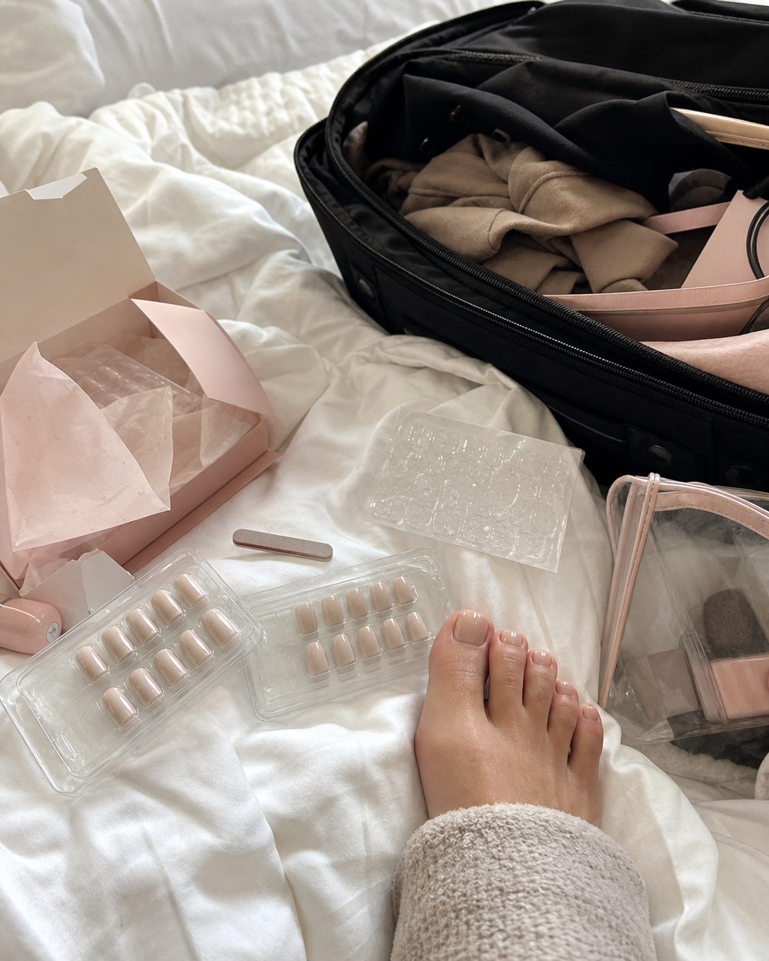 Messy bed unboxing phone photo with neutral press-on nail trays